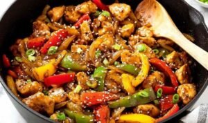 One-pot black pepper chicken with tender chicken breast cubes, red and yellow bell peppers in a glossy sweet and spicy sauce garnished with sesame seeds and green onions