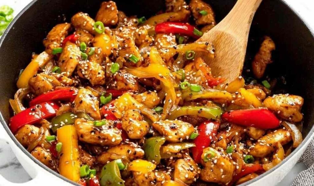 One-pot black pepper chicken with tender chicken breast cubes, red and yellow bell peppers in a glossy sweet and spicy sauce garnished with sesame seeds and green onions