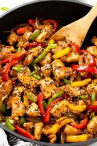 One-pot black pepper chicken with tender chicken breast cubes, red and yellow bell peppers in a glossy sweet and spicy sauce garnished with sesame seeds and green onions