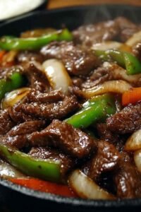 A bowl of Chinese Pepper Steak with Onions served over steamed jasmine rice with a glossy savory soy and hoisin sauce