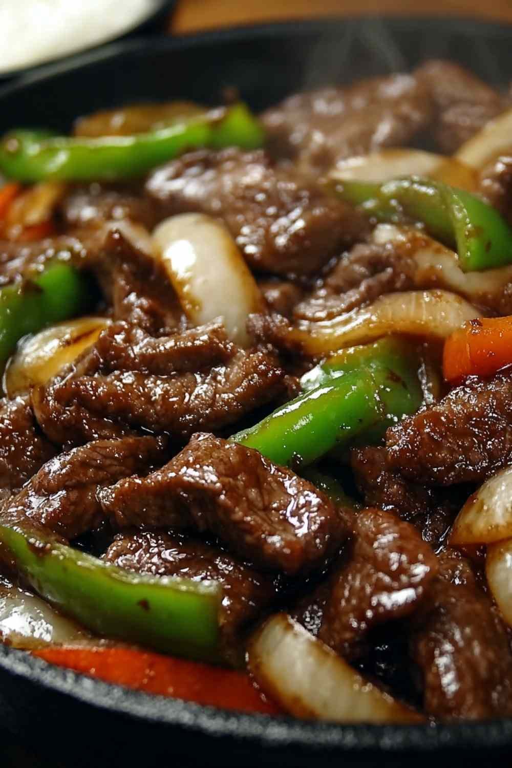 A bowl of Chinese Pepper Steak with Onions served over steamed jasmine rice with a glossy savory soy and hoisin sauce