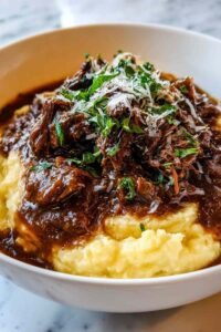 Short Rib Ragu with Parmesan Mashed Potatoes served on a white plate garnished with fresh parsley