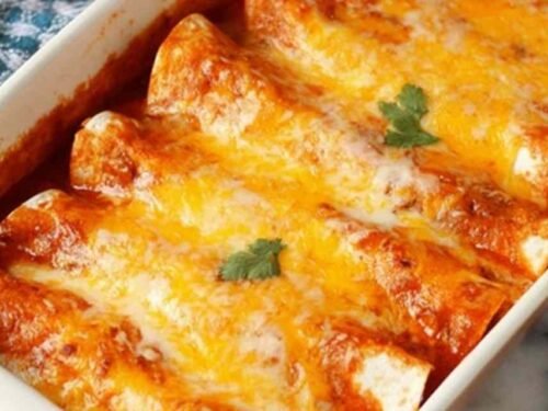 A baking dish of 5 Ingredient Beef Enchiladas covered in melted cheese and red enchilada sauce, fresh from the oven