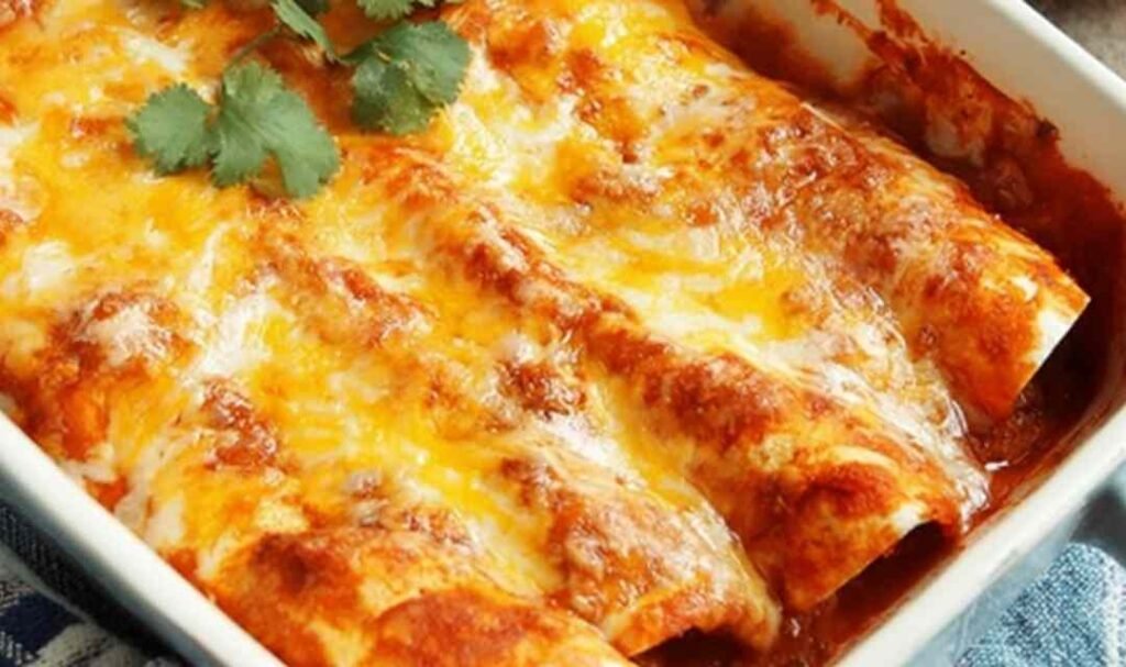A baking dish of 5 Ingredient Beef Enchiladas covered in melted cheese and red enchilada sauce, fresh from the oven