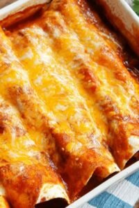 A baking dish of 5 Ingredient Beef Enchiladas covered in melted cheese and red enchilada sauce, fresh from the oven
