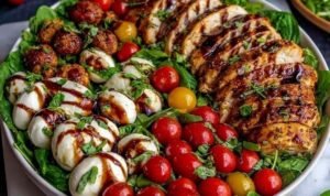 Baked marinated chicken salad with mozzarella balls, cherry tomatoes, avocado, and balsamic vinaigrette on a white plate