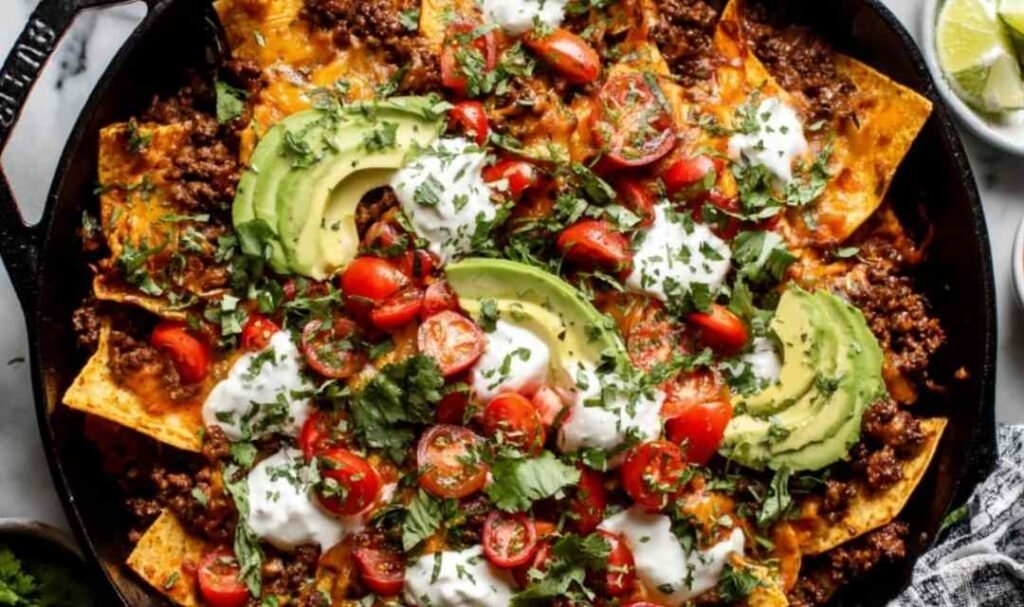 Beef skillet enchiladas in a cast iron skillet topped with melted cheese, avocado slices, and fresh cilantro