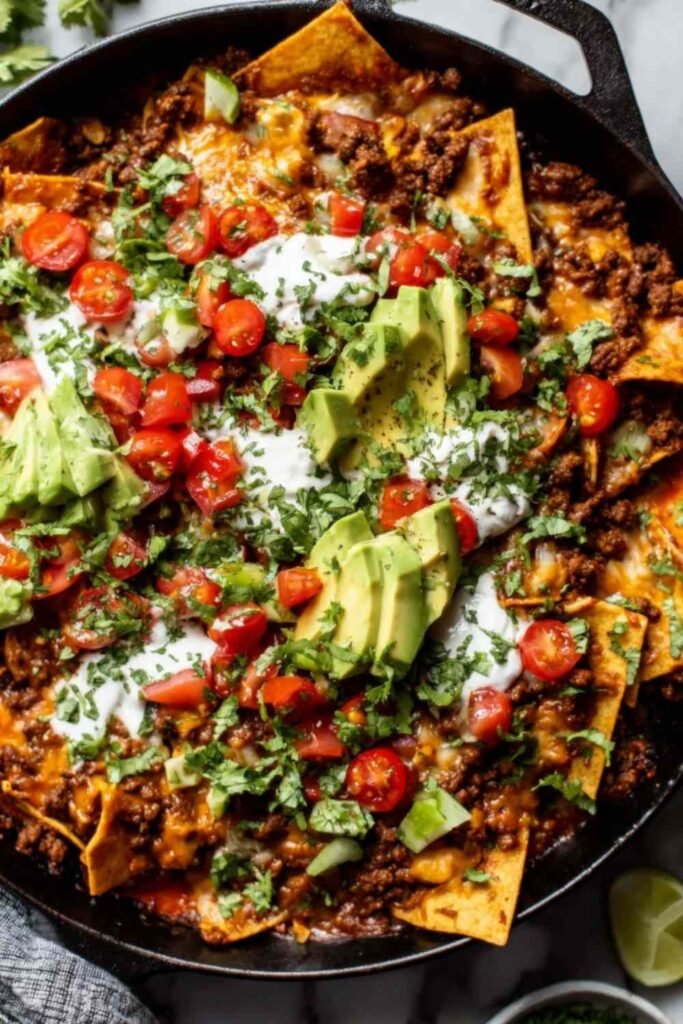 Beef skillet enchiladas in a cast iron skillet topped with melted cheese, avocado slices, and fresh cilantro
