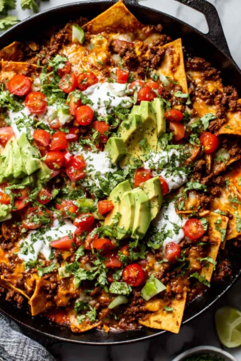 Beef skillet enchiladas in a cast iron skillet topped with melted cheese, avocado slices, and fresh cilantro