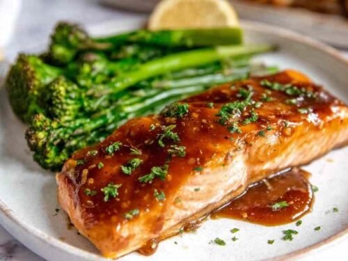 Four baked salmon fillets with honey garlic glaze arranged skin side down in a parchment-lined baking dish