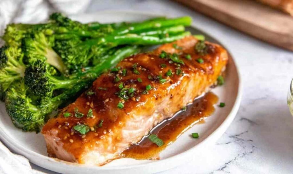 Four baked salmon fillets with honey garlic glaze arranged skin side down in a parchment-lined baking dish