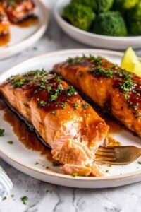 Four baked salmon fillets with honey garlic glaze arranged skin side down in a parchment-lined baking dish
