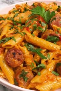 Creamy Cajun sausage pasta in a large skillet with smoky sausage rounds, colorful bell peppers, and fresh parsley garnish