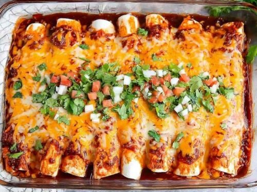 A pan of baked chicken enchiladas covered in melted cheese and red enchilada sauce, garnished with fresh cilantro and a dollop of sour cream