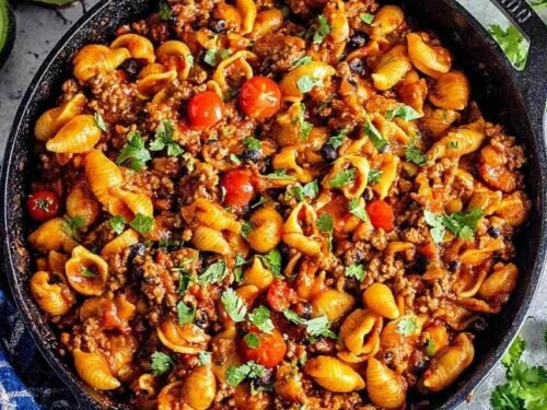 One pot taco pasta recipe simmering in a Dutch oven with ground beef, salsa, corn, and shell pasta absorbing the seasoned broth