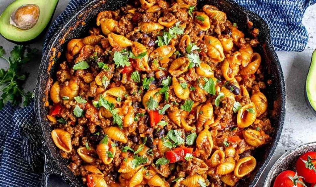 One pot taco pasta recipe simmering in a Dutch oven with ground beef, salsa, corn, and shell pasta absorbing the seasoned broth