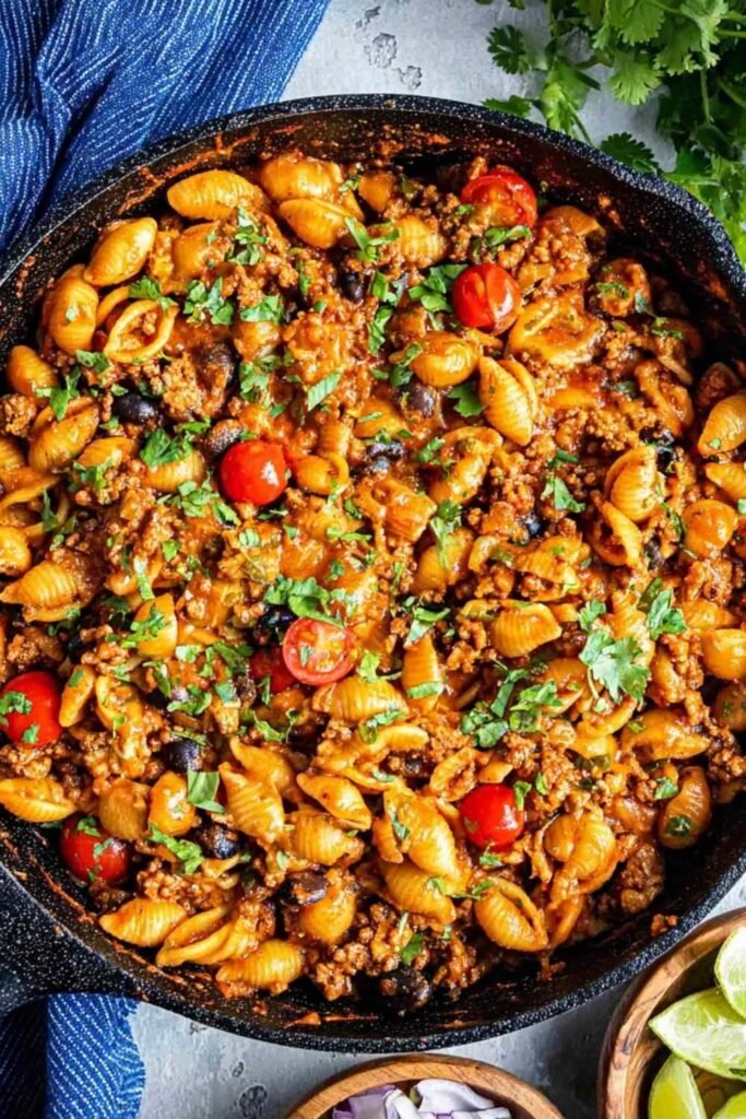 One pot taco pasta recipe simmering in a Dutch oven with ground beef, salsa, corn, and shell pasta absorbing the seasoned broth