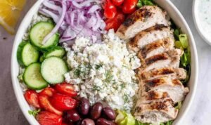 Greek Chicken Bowls Greek chicken bowls with sliced lemon herb marinated chicken breast, romaine, cherry tomatoes, cucumber, kalamata olives, tzatziki, and feta cheese