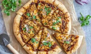Freshly baked BBQ chicken pizza with shredded chicken, smoked Gouda, mozzarella, red onion, and cilantro on a golden crispy crust