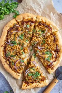 Freshly baked BBQ chicken pizza with shredded chicken, smoked Gouda, mozzarella, red onion, and cilantro on a golden crispy crust