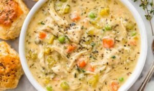 Close-up bowl of chicken pot pie soup with shredded chicken, potatoes, peas, and carrots in a creamy broth topped with fresh parsley