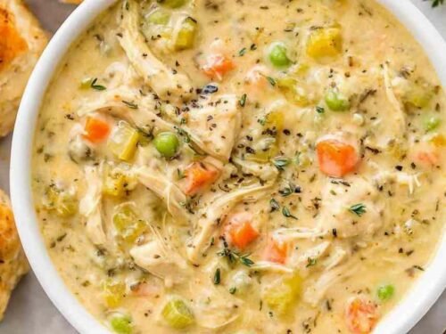 Close-up bowl of chicken pot pie soup with shredded chicken, potatoes, peas, and carrots in a creamy broth topped with fresh parsley