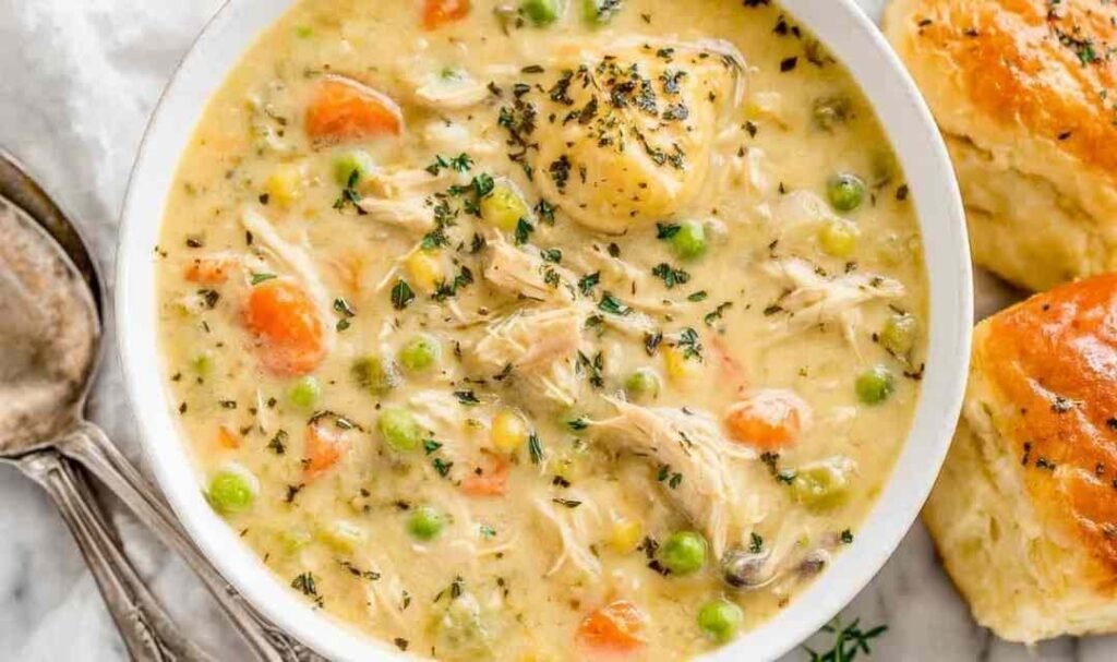 Close-up bowl of chicken pot pie soup with shredded chicken, potatoes, peas, and carrots in a creamy broth topped with fresh parsley