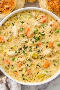 Close-up bowl of chicken pot pie soup with shredded chicken, potatoes, peas, and carrots in a creamy broth topped with fresh parsley
