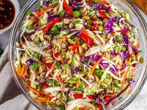 A large bowl of Chinese chicken salad with shredded chicken, red cabbage, carrots, and sesame ginger dressing