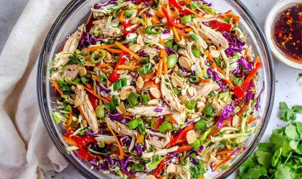 A large bowl of Chinese chicken salad with shredded chicken, red cabbage, carrots, and sesame ginger dressing
