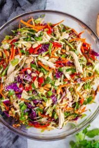 A large bowl of Chinese chicken salad with shredded chicken, red cabbage, carrots, and sesame ginger dressing