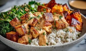 Healthy chicken sweet potato bowls with roasted sweet potatoes, pan-seared chicken, rice, and creamy spiced sauce in a white bowl