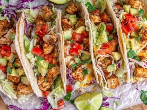 Overhead view of chicken tacos filled with seasoned chopped chicken, shredded lettuce, tomato, red onion, and avocado in flour tortillas