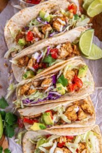 Overhead view of chicken tacos filled with seasoned chopped chicken, shredded lettuce, tomato, red onion, and avocado in flour tortillas