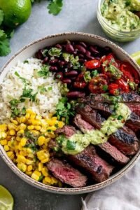 Cilantro lime steak bowl with sliced grilled flank steak, avocado, black beans, corn, and cherry tomatoes over white rice