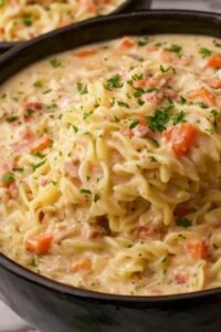 Close-up bowl of crack chicken noodle soup topped with crumbled bacon and shredded cheddar cheese