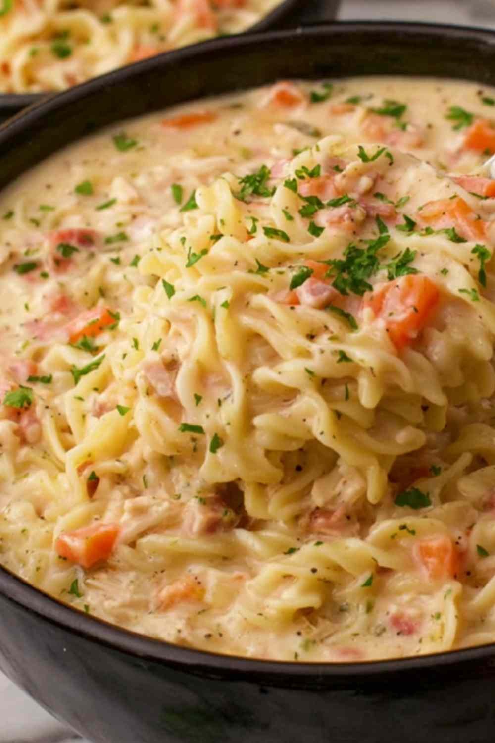 Close-up bowl of crack chicken noodle soup topped with crumbled bacon and shredded cheddar cheese
