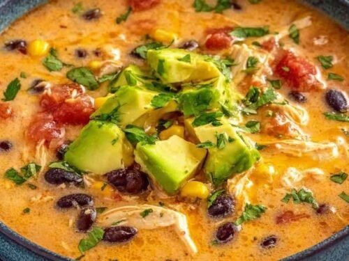 Bowl of creamy chicken enchilada soup topped with shredded cheese, sour cream, and fresh cilantro