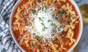 A bowl of lasagna soup topped with ricotta cheese, shredded mozzarella, and grated Parmesan