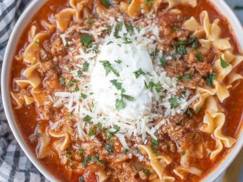 A bowl of lasagna soup topped with ricotta cheese, shredded mozzarella, and grated Parmesan