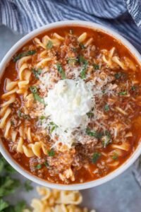 A bowl of lasagna soup topped with ricotta cheese, shredded mozzarella, and grated Parmesan