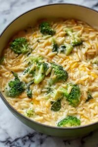 Creamy one-pot broccoli cheddar orzo in a large pot topped with extra shredded cheddar and black pepper