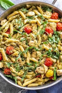 Easy chicken pesto pasta with cherry tomatoes and spinach tossed in a skillet with basil pesto