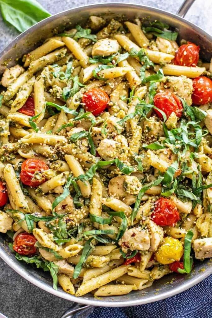 Easy chicken pesto pasta with cherry tomatoes and spinach tossed in a skillet with basil pesto
