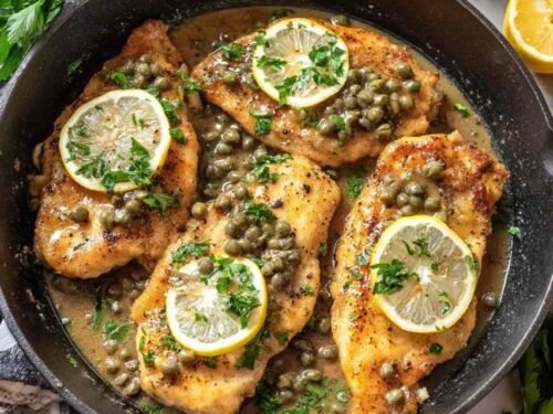 Homemade Chicken Piccata served on a white plate with lemon slices, capers, and fresh parsley garnish