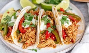 Crockpot chicken fajitas with juicy shredded chicken, red and yellow bell peppers, and onions in a slow cooker