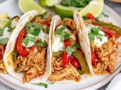 Crockpot chicken fajitas with juicy shredded chicken, red and yellow bell peppers, and onions in a slow cooker