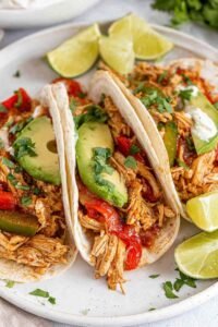 Crockpot chicken fajitas with juicy shredded chicken, red and yellow bell peppers, and onions in a slow cooker