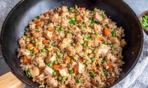 Chicken fried rice with tender chicken breast, scrambled eggs, peas and carrots cooking in a large skillet