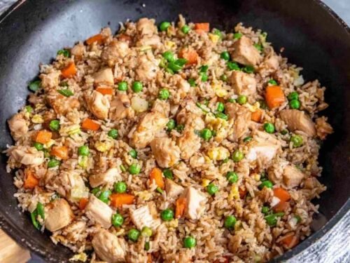 Chicken fried rice with tender chicken breast, scrambled eggs, peas and carrots cooking in a large skillet